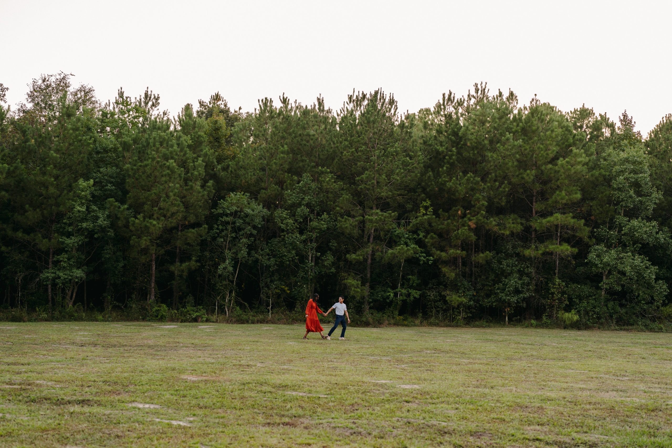 A couple walking across an open field for their engagement pictures done by Angelina Loreta Photography in Houston, Texas