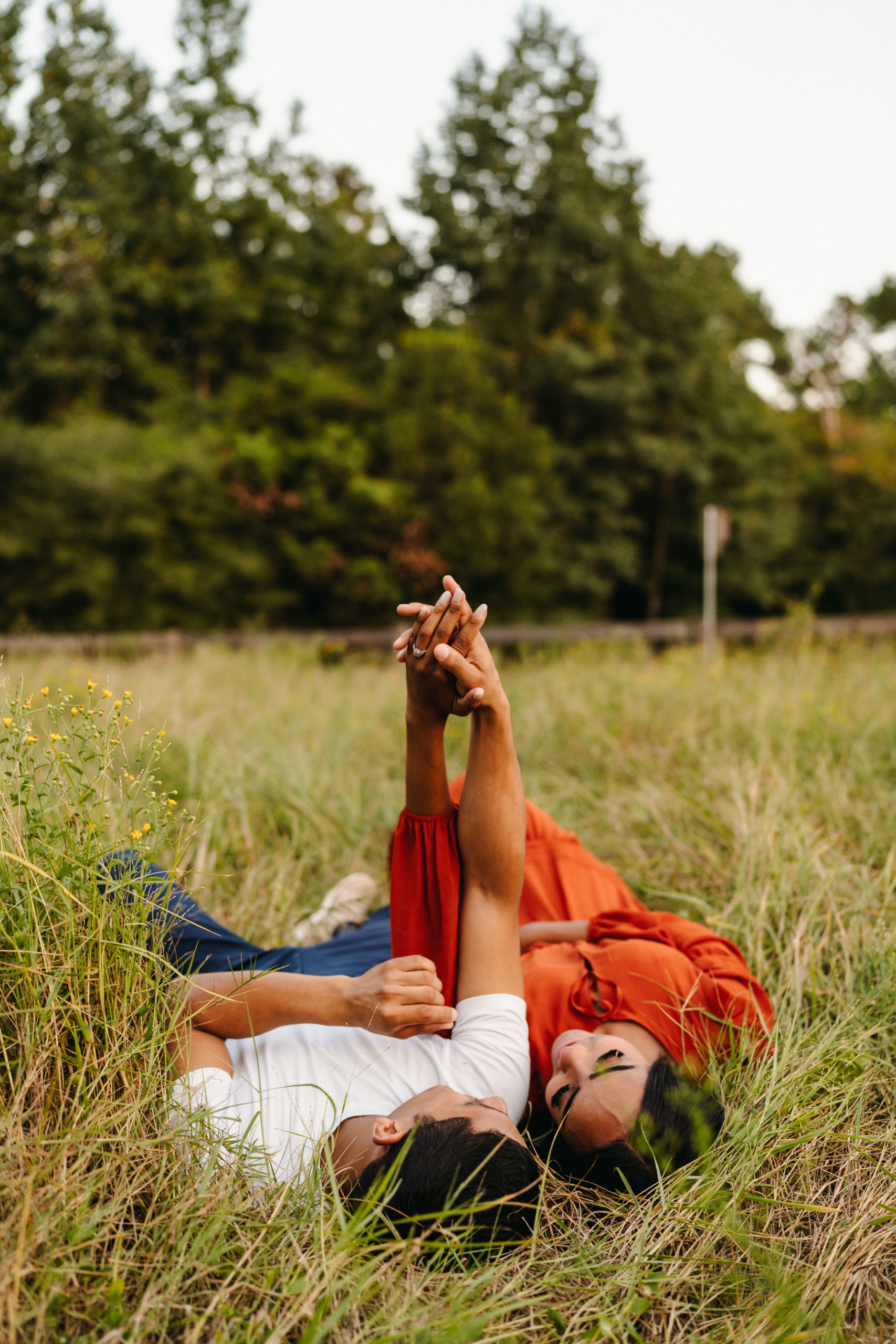 A couple lying down in a tall grass field for their engagement pictures done by Angelina Loreta Photography in Houston, Texas.