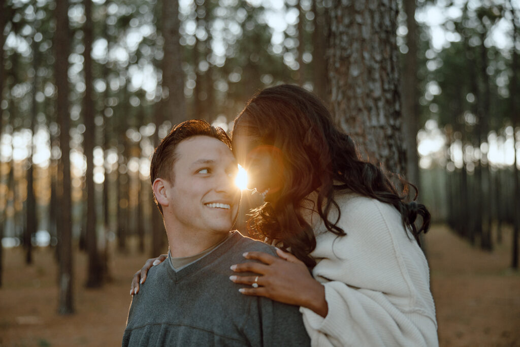 couple smiling with the sun peeking through during engagement shoot