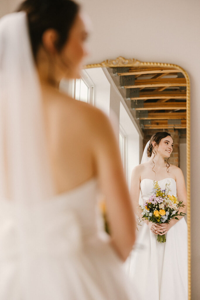 bride looking at her reflection in large gold mirror