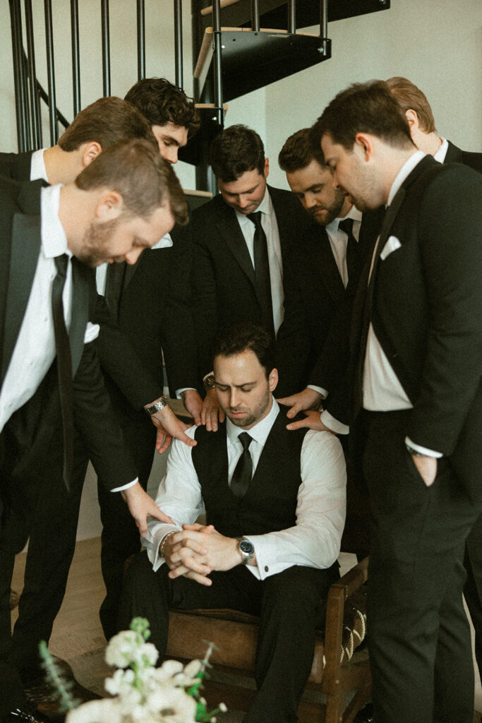 groomsmen praying over groom getting ready wedding photos