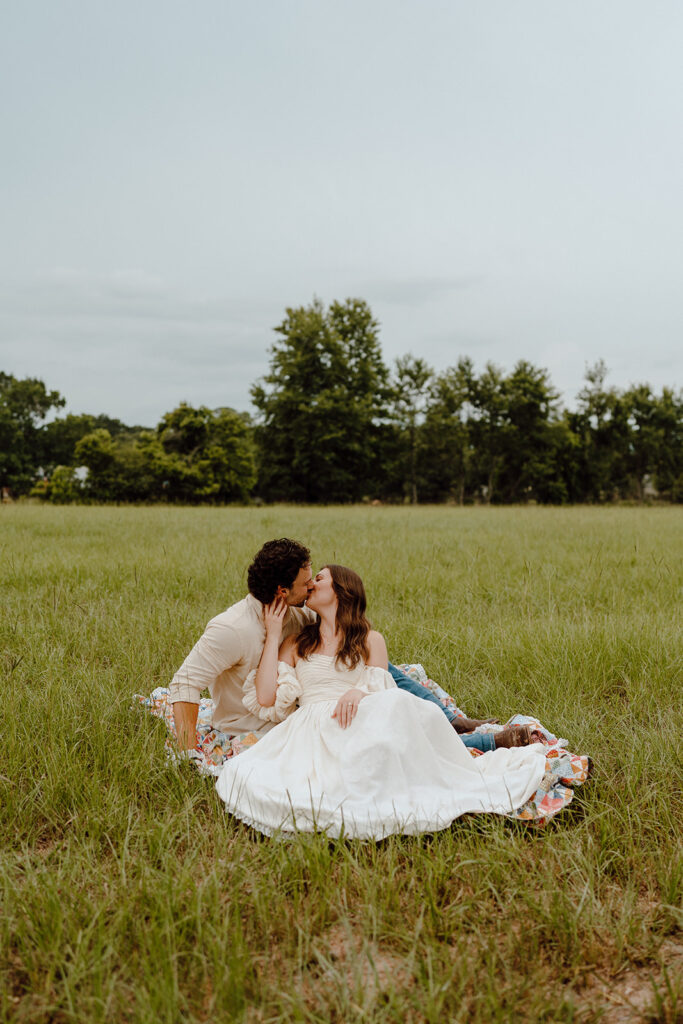 couple sitting in field pose and kissing
