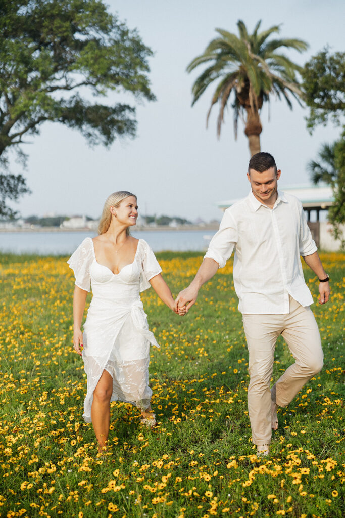 couple smiling and walking in yellow flower field with palm trees in background