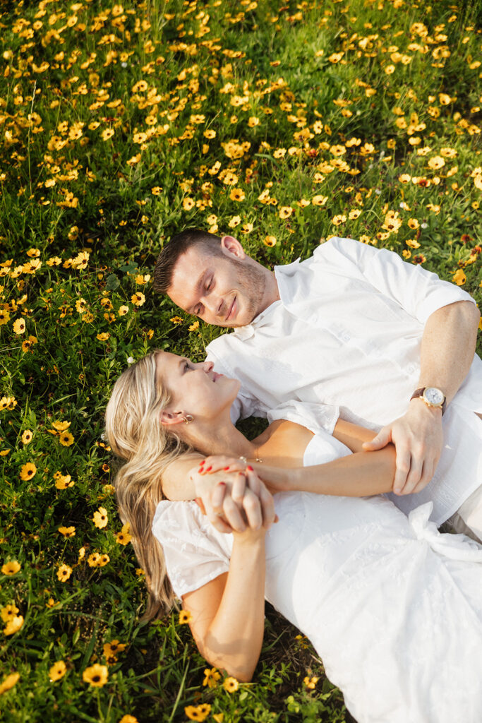 couple smiling and laying down in yellow flower field