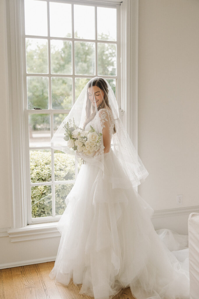 wedding photos in front of window with bride holding bouquet under veil