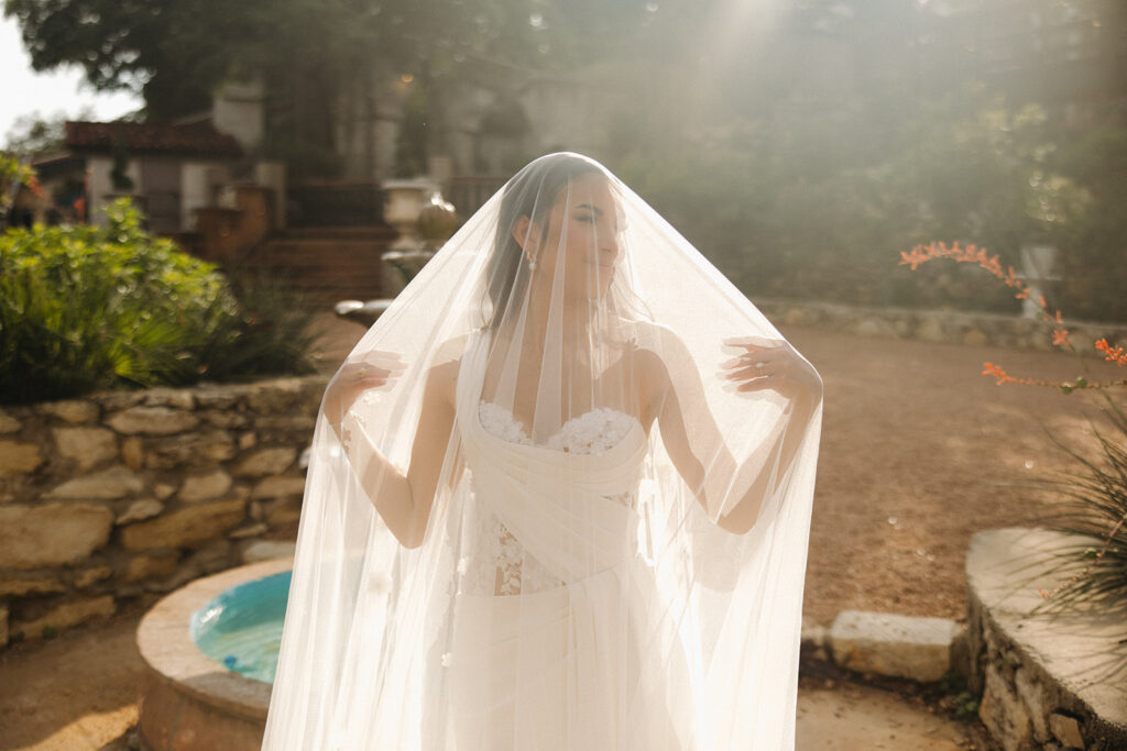 bride underneath veil in front of fountain