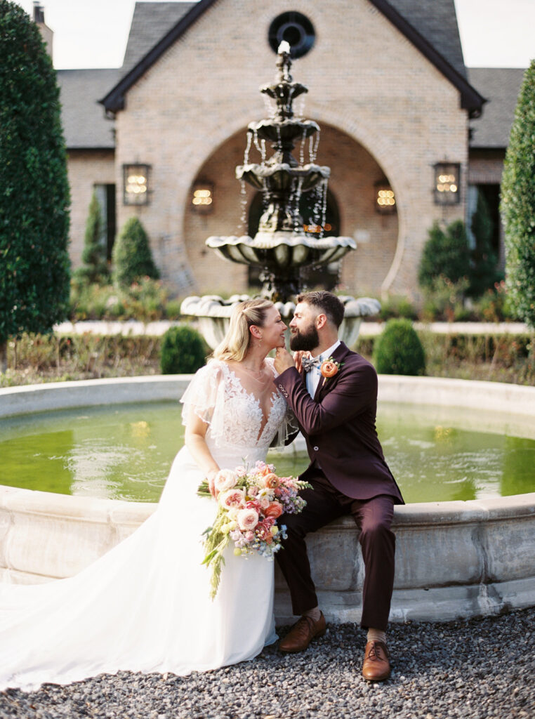 bride and groom sitting in front of a fountain for wedding photos