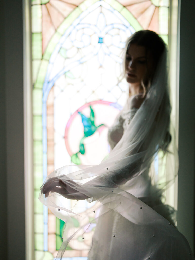 bride posing in front of stained glass window with her veil