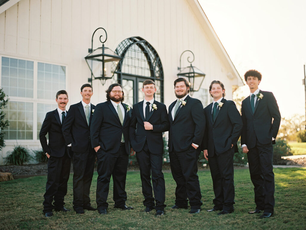 groomsmen in suits standing in front of the camp hosea wedding venue