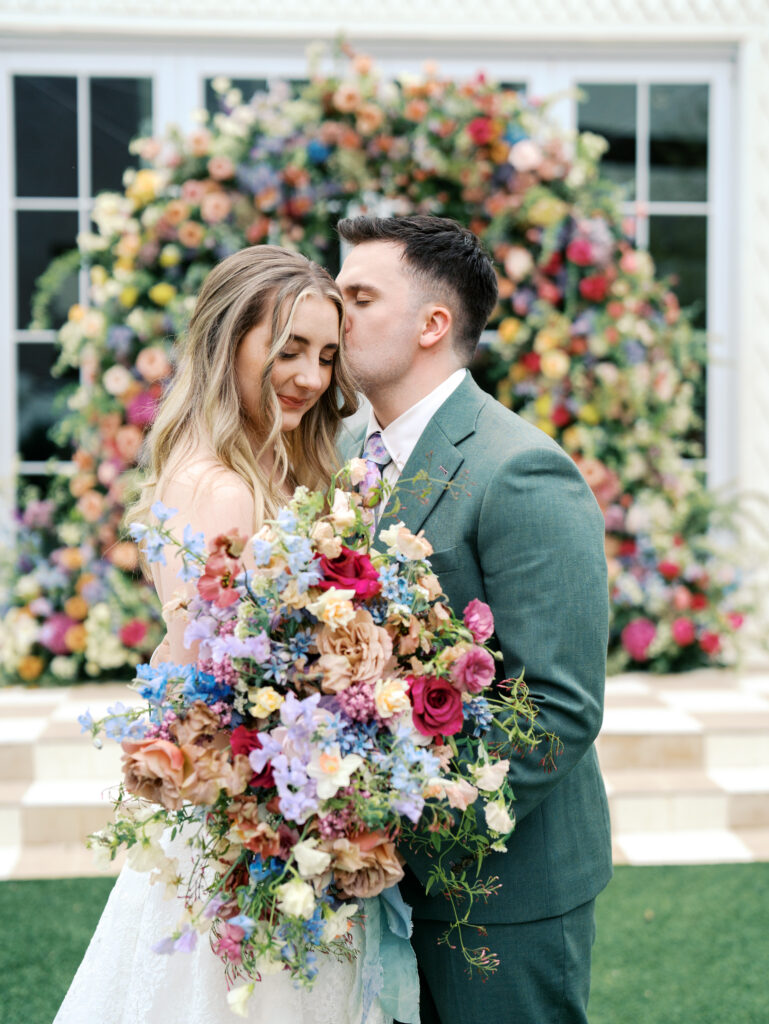 groom kissing bride cheek with lots of florals