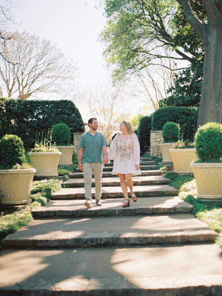 man and woman walking surrounded by greenery for a Texas engagement session Dreamy Outdoor Engagement Photos in Botanical Gardens