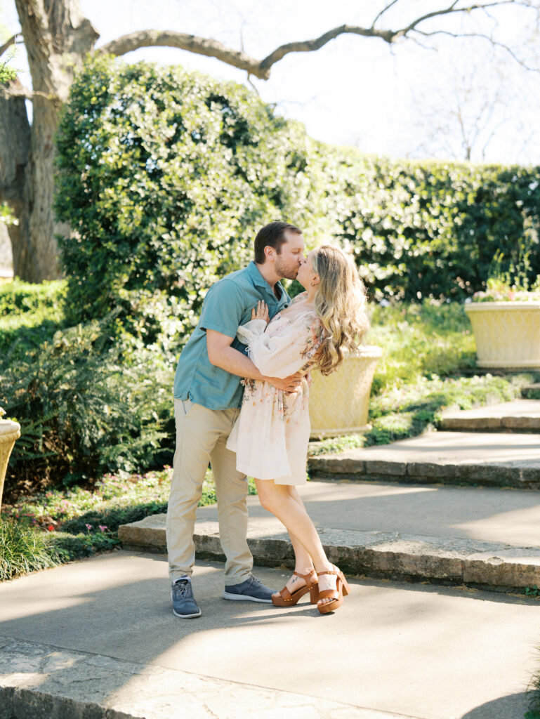 man kissing woman surrounded by greenery for their garden engagement session