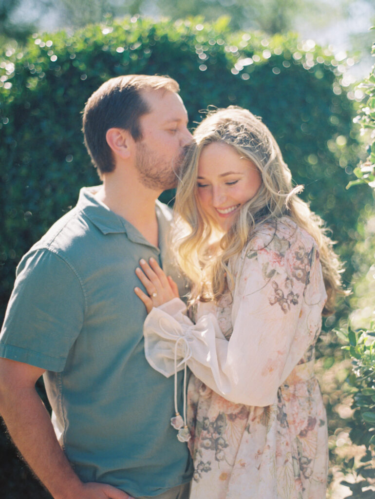 man kissing woman surrounded by greenery for their garden engagement session 