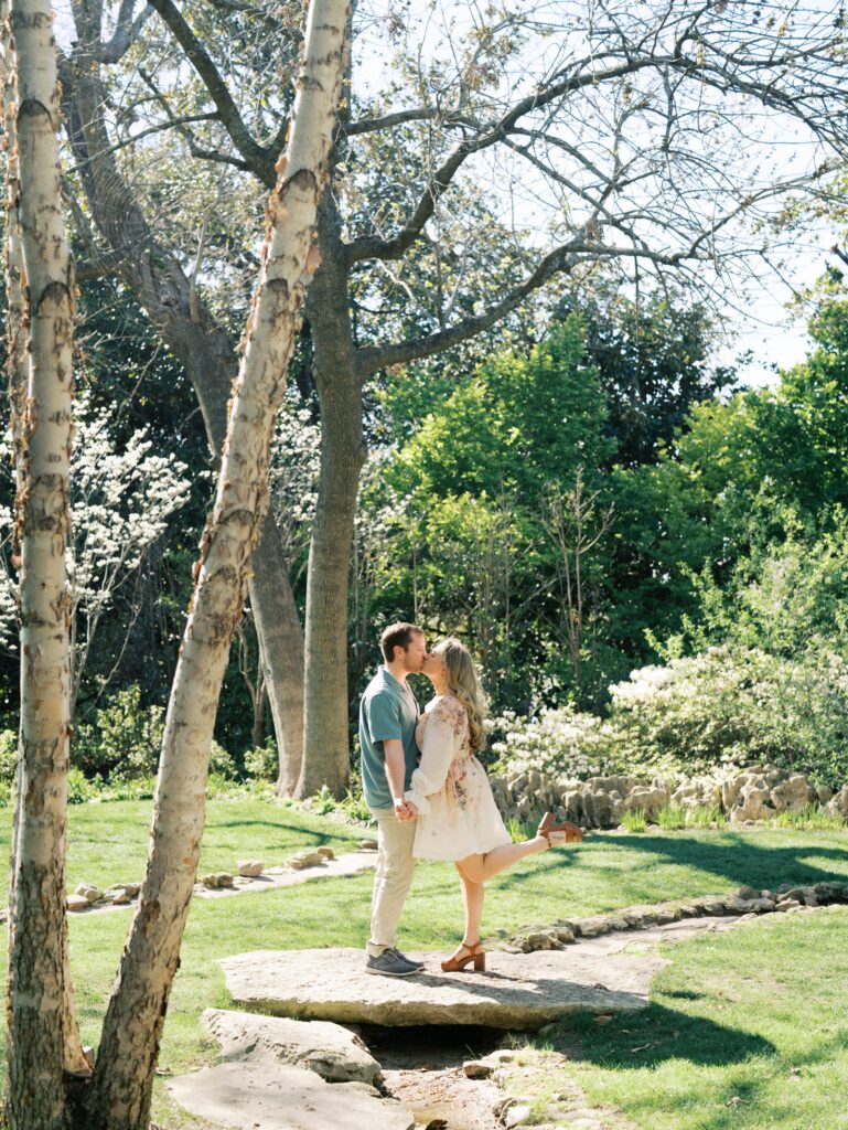 man and woman kissing in garden engagement session surrounded by greenery 