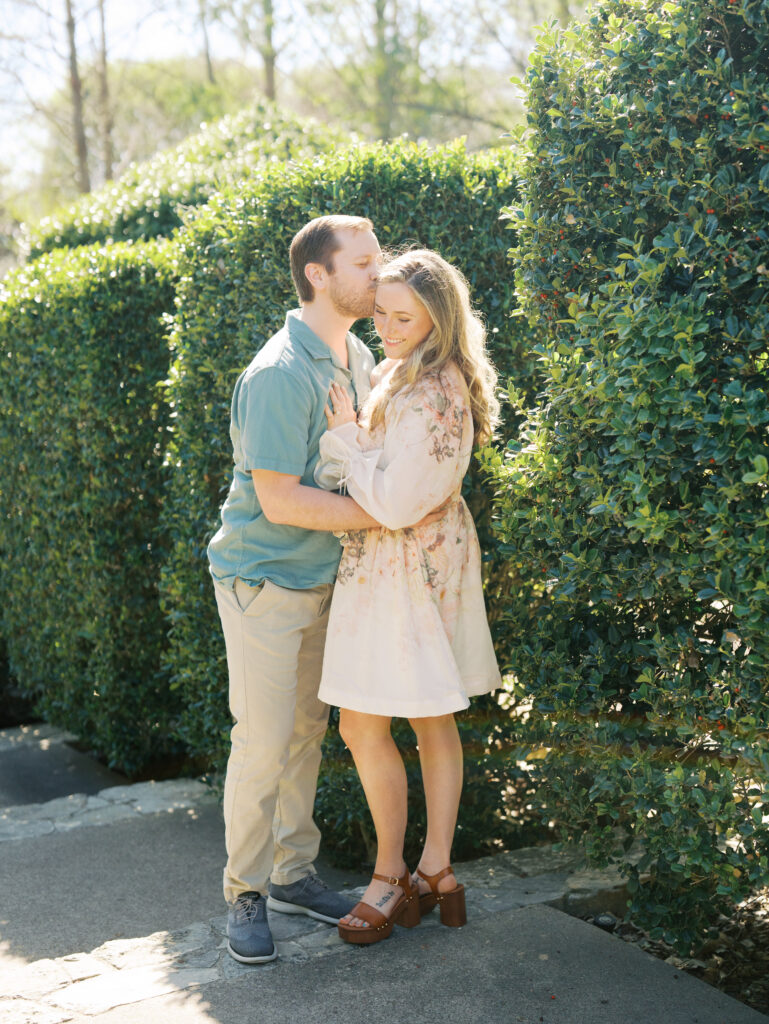man kissing woman surrounded by greenery for their garden engagement session