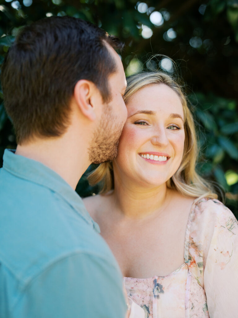 couple smiling cheek to cheek surrounded by florals for their engagement session