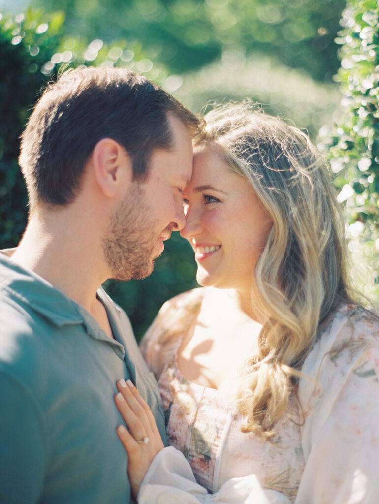 man and woman candidly smiling nose to nose for their garden engagement session