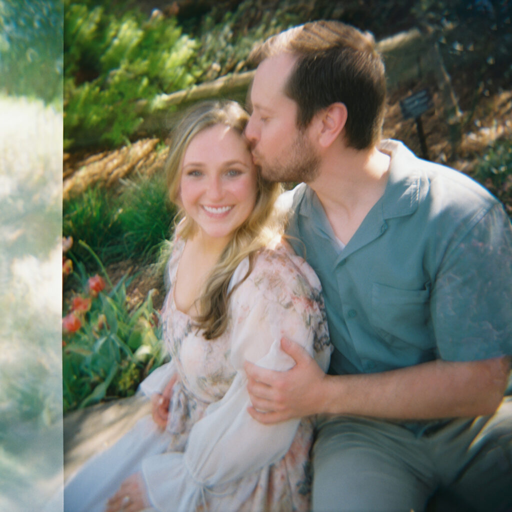 man kissing woman surrounded by greenery for their garden engagement session