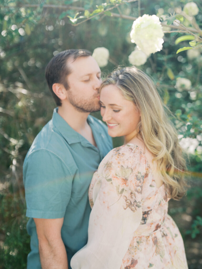 man kissing woman during Texas garden engagement session surrounded by greenery 
