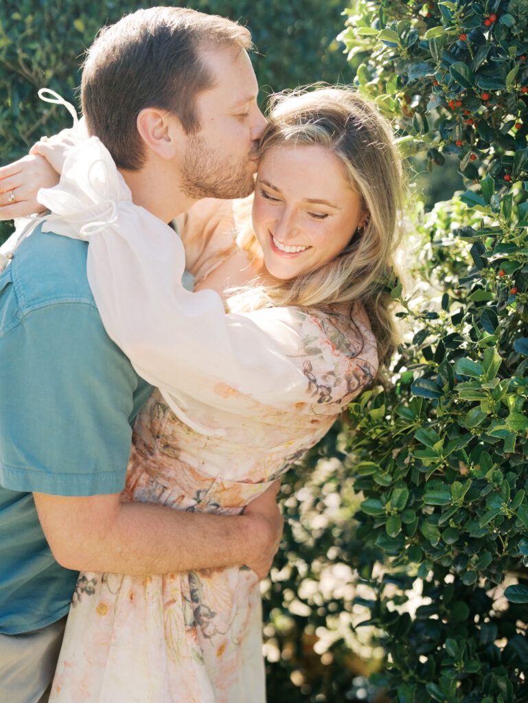 man kissing woman surrounded by greenery for their garden engagement session