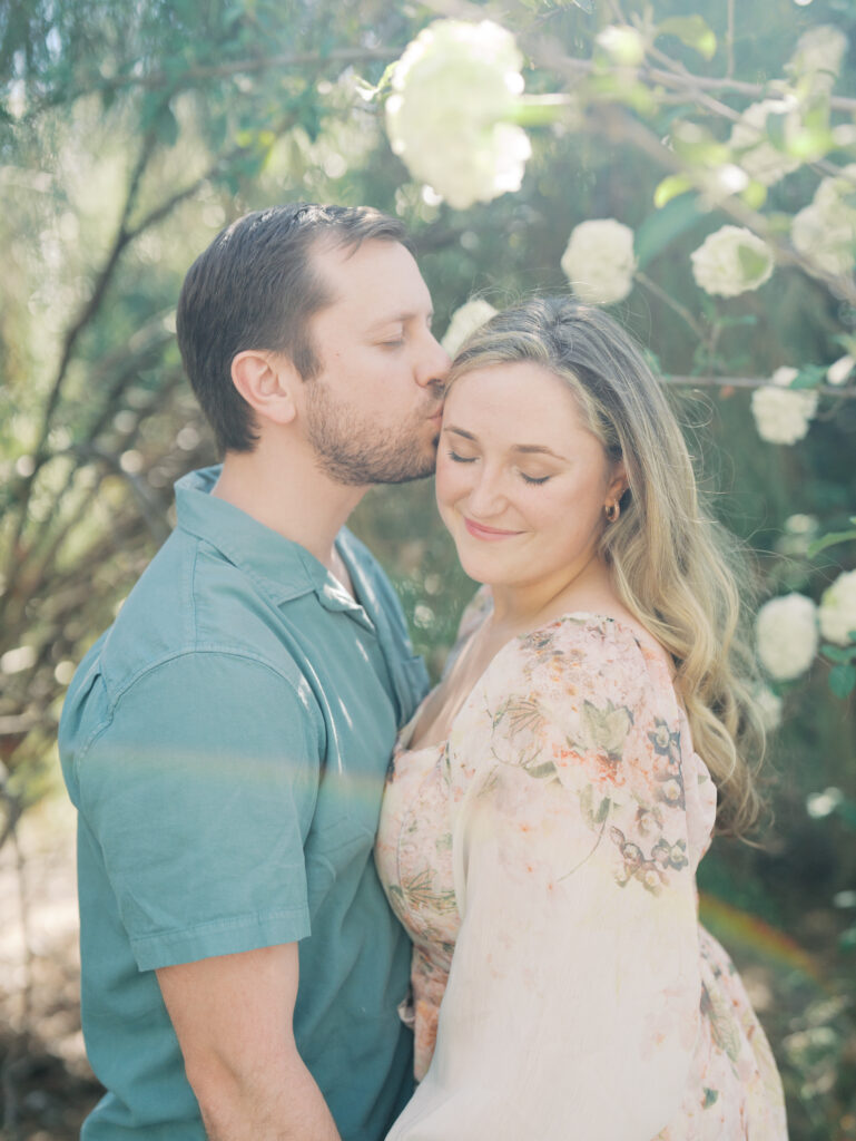couple smiling cheek to cheek surrounded by florals for their engagement session 