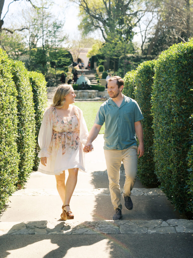 couple walking and smiling surrounded by greenery for their spring engagement session
