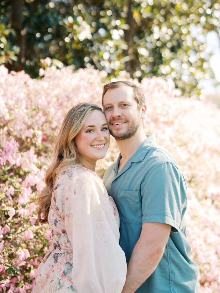 couple smiling cheek to cheek surrounded by florals for their engagement session 