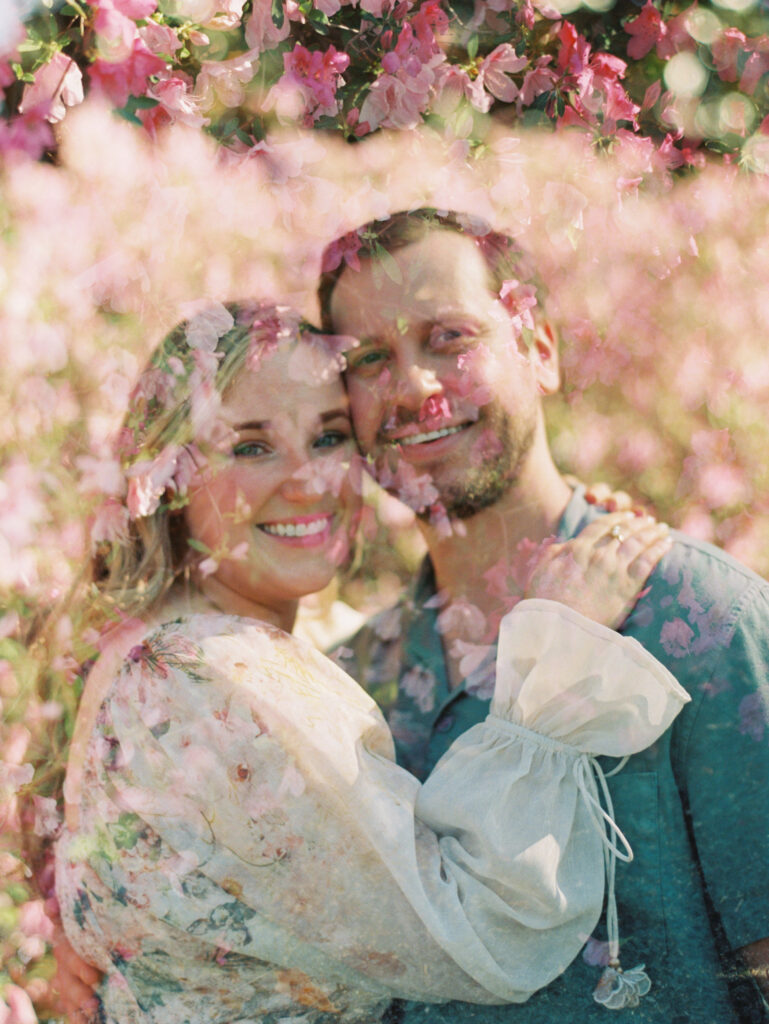 man and woman smiling together with pink flowers garden engagement session 