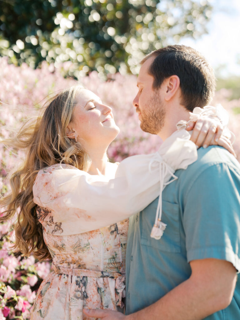 man and woman candidly smiling towards each other during garden engagement session