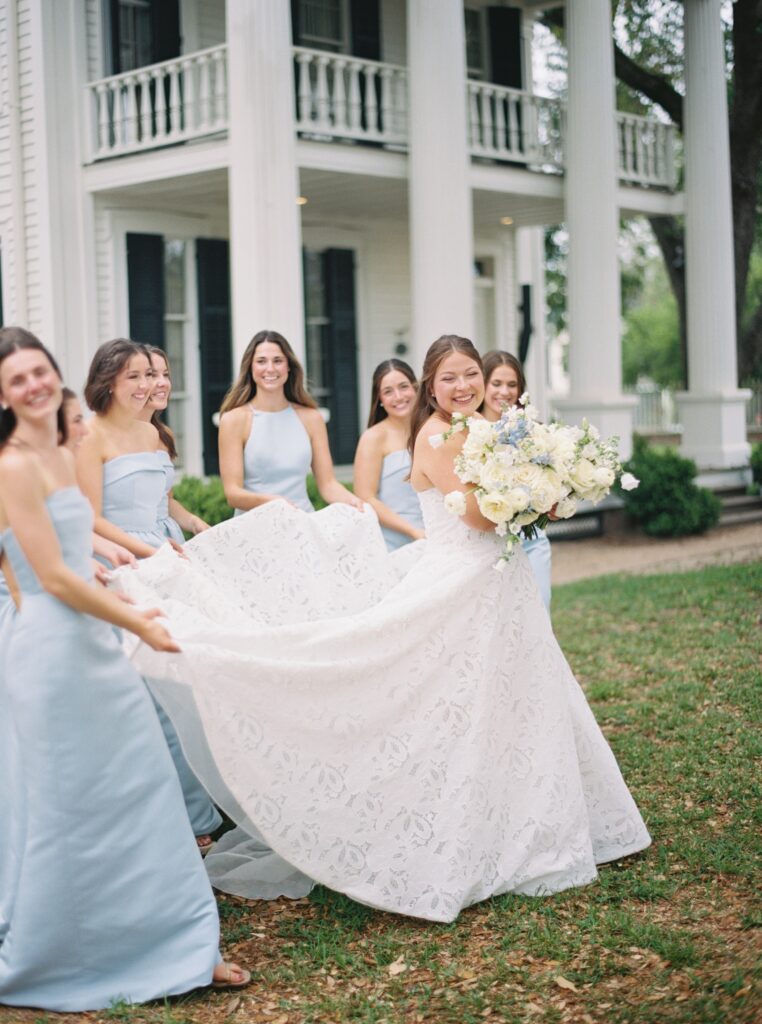 bridesmaids and bride on wedding day smiling and holding brides dress 