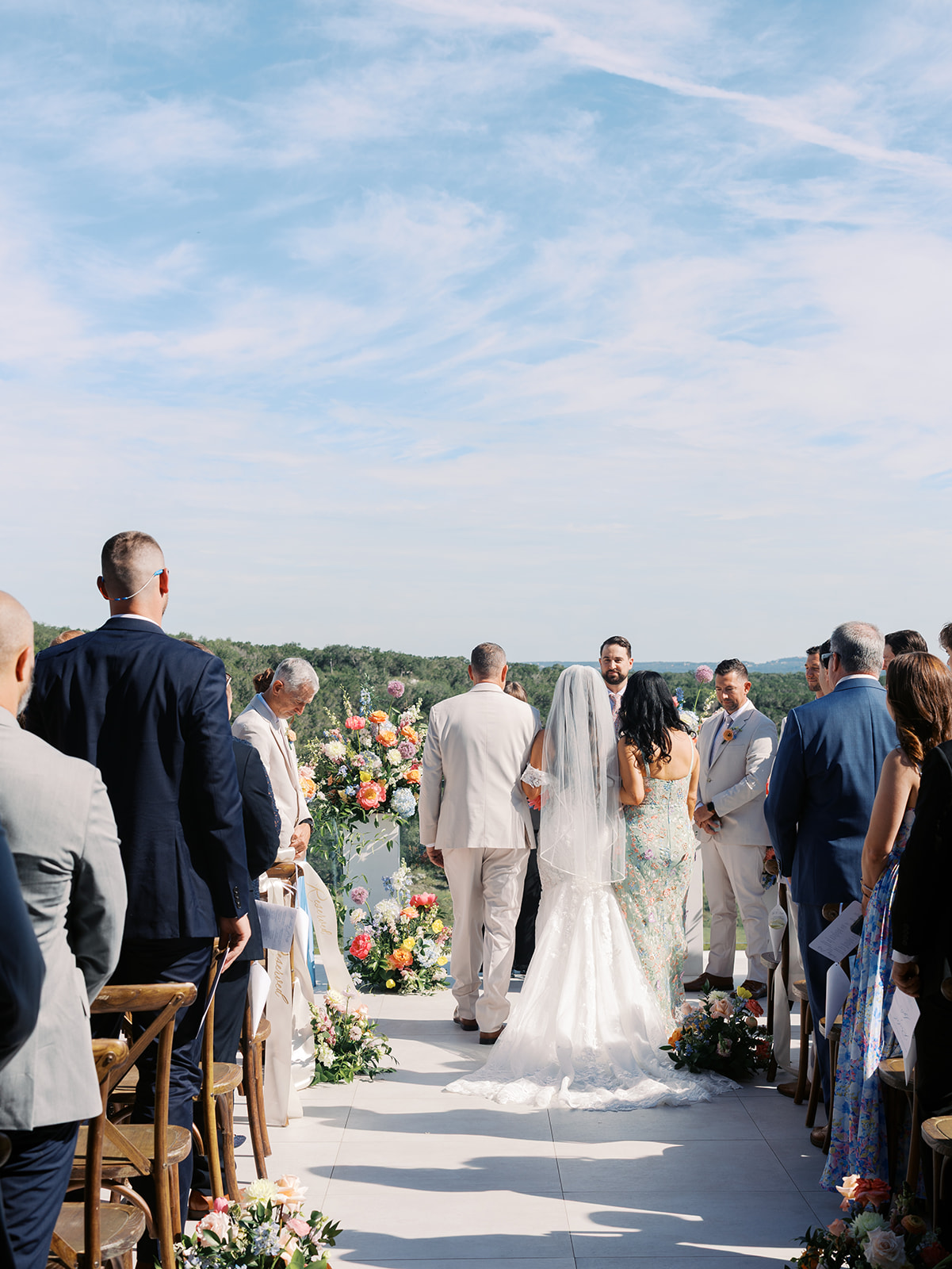 A couple kisses at an outdoor wedding ceremony as guests watch. The setting features floral arrangements and a scenic landscape in the background for a wedding in austin tx
