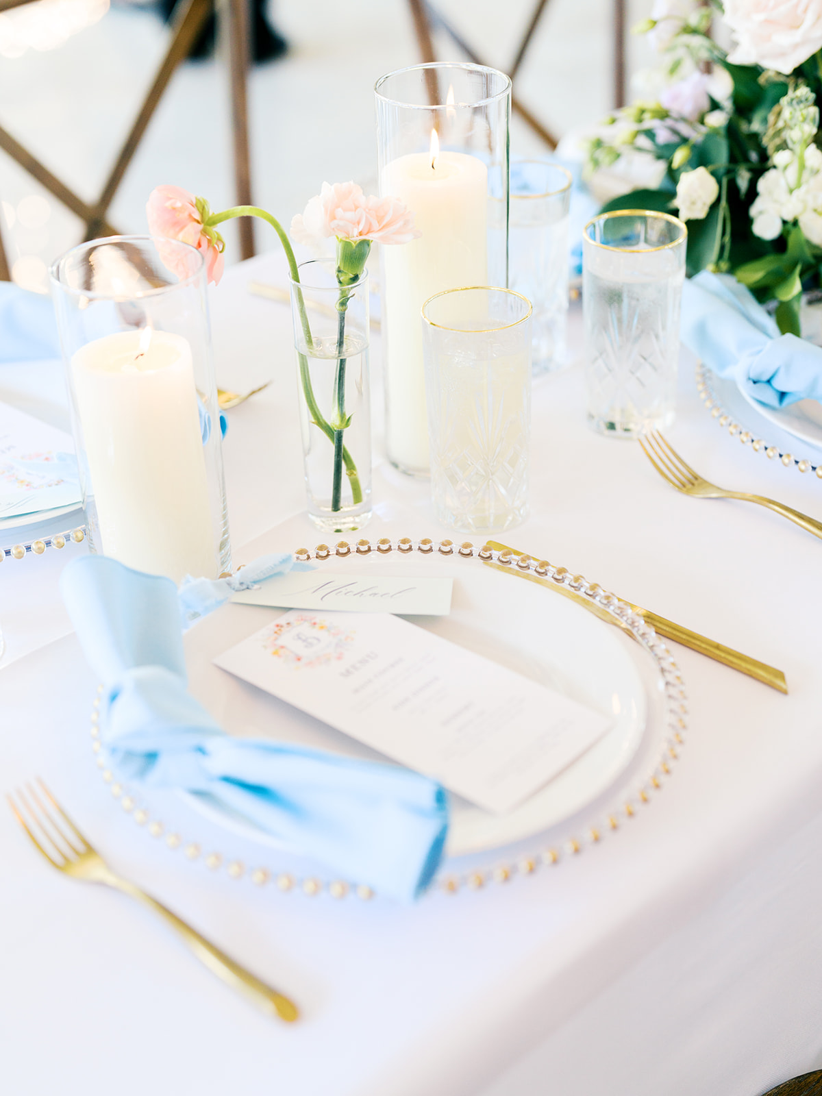 Elegant table setting with white tablecloth, gold utensils, blue napkins, candles, and pastel flower centerpieces at a formal event for a wedding in austin tx