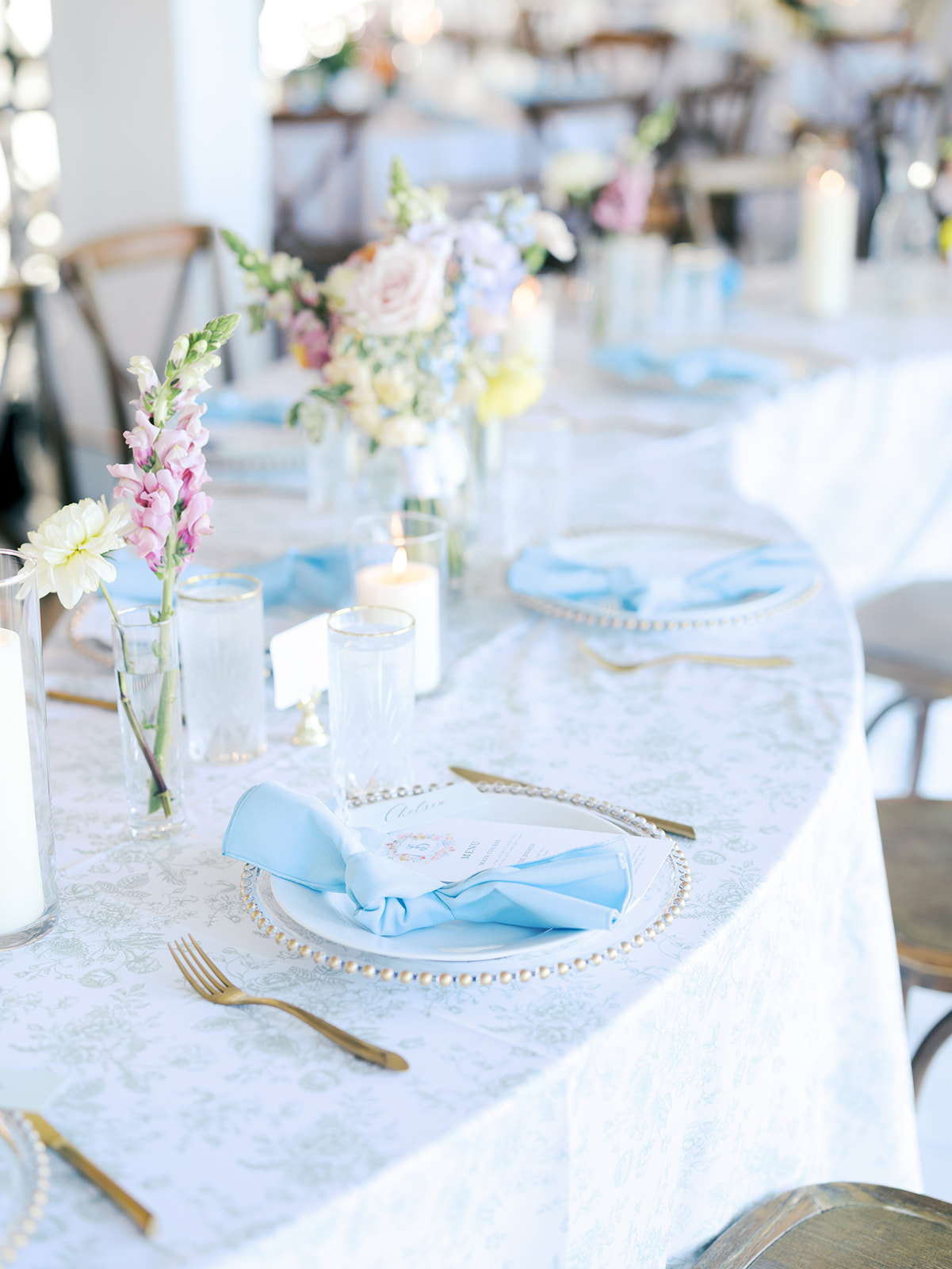 Elegant table setting with white tablecloth, gold utensils, blue napkins, candles, and pastel flower centerpieces at a formal event for a wedding in austin tx
