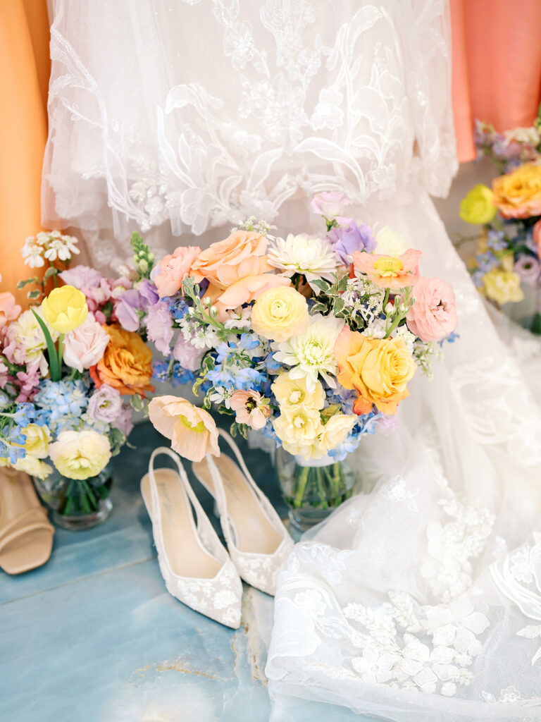 Cosmetic products, a gold box, and a mirror are arranged on a white surface with yellow and peach flowers and scattered flower petals.