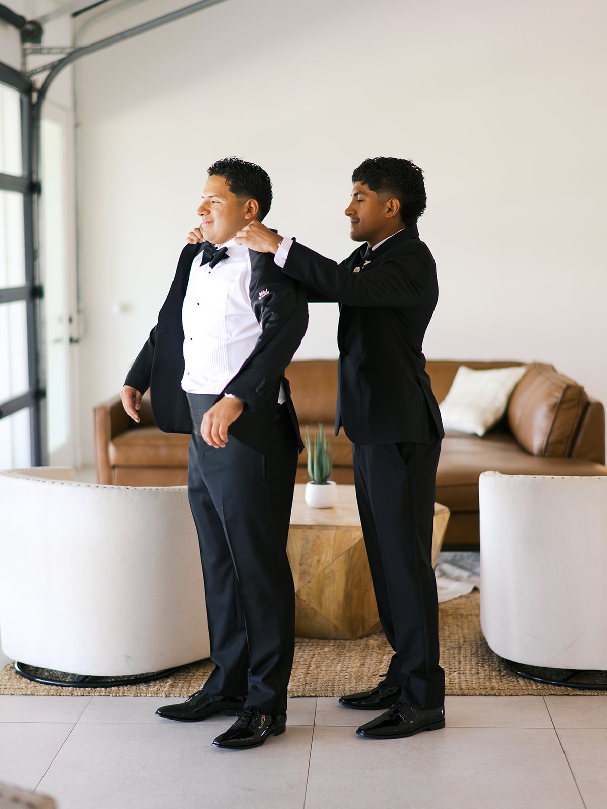 A man in formal attire adjusts his bow tie while others in suits stand nearby in a room.