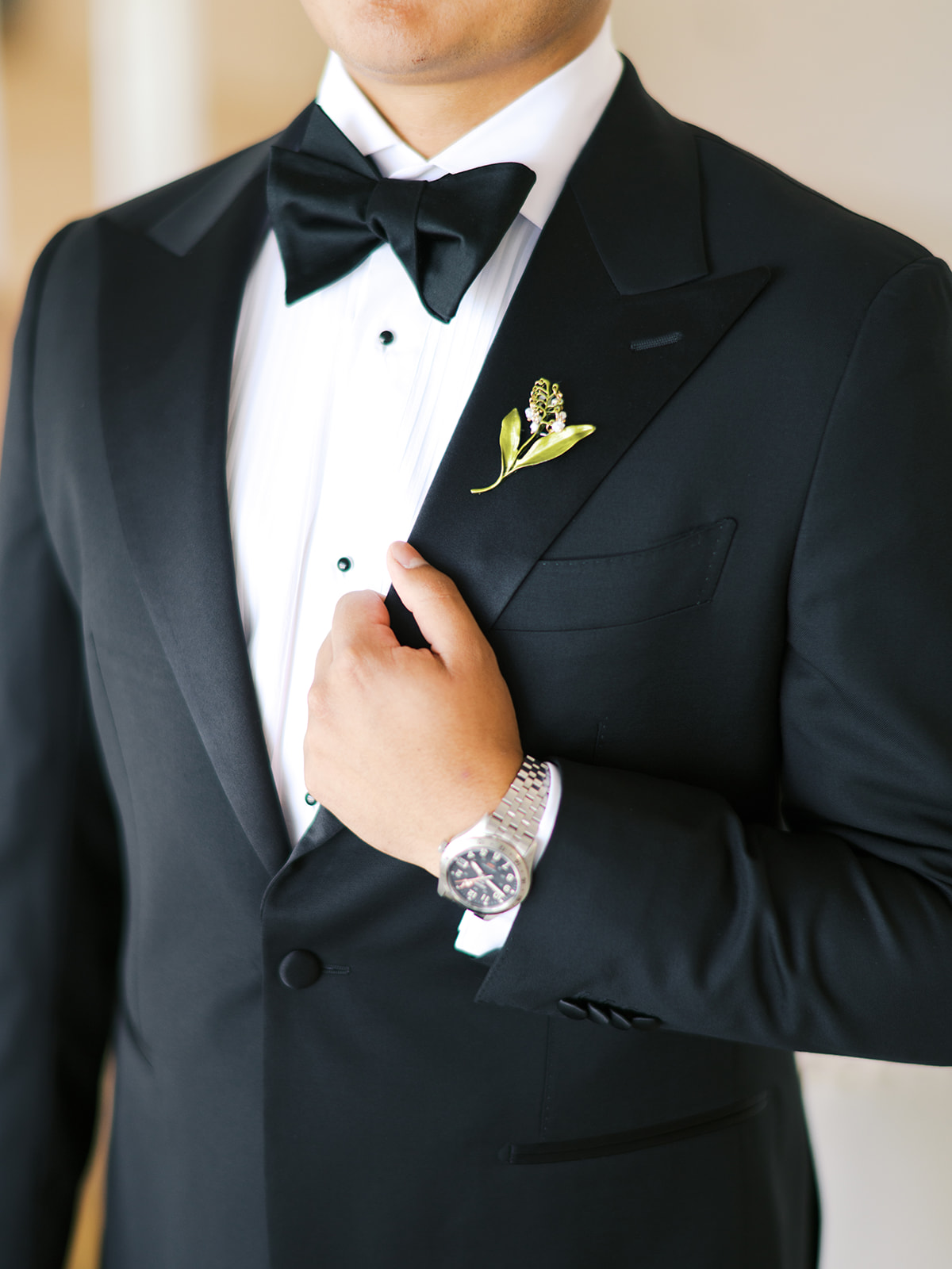 A man in formal attire adjusts his bow tie while others in suits stand nearby in a room.