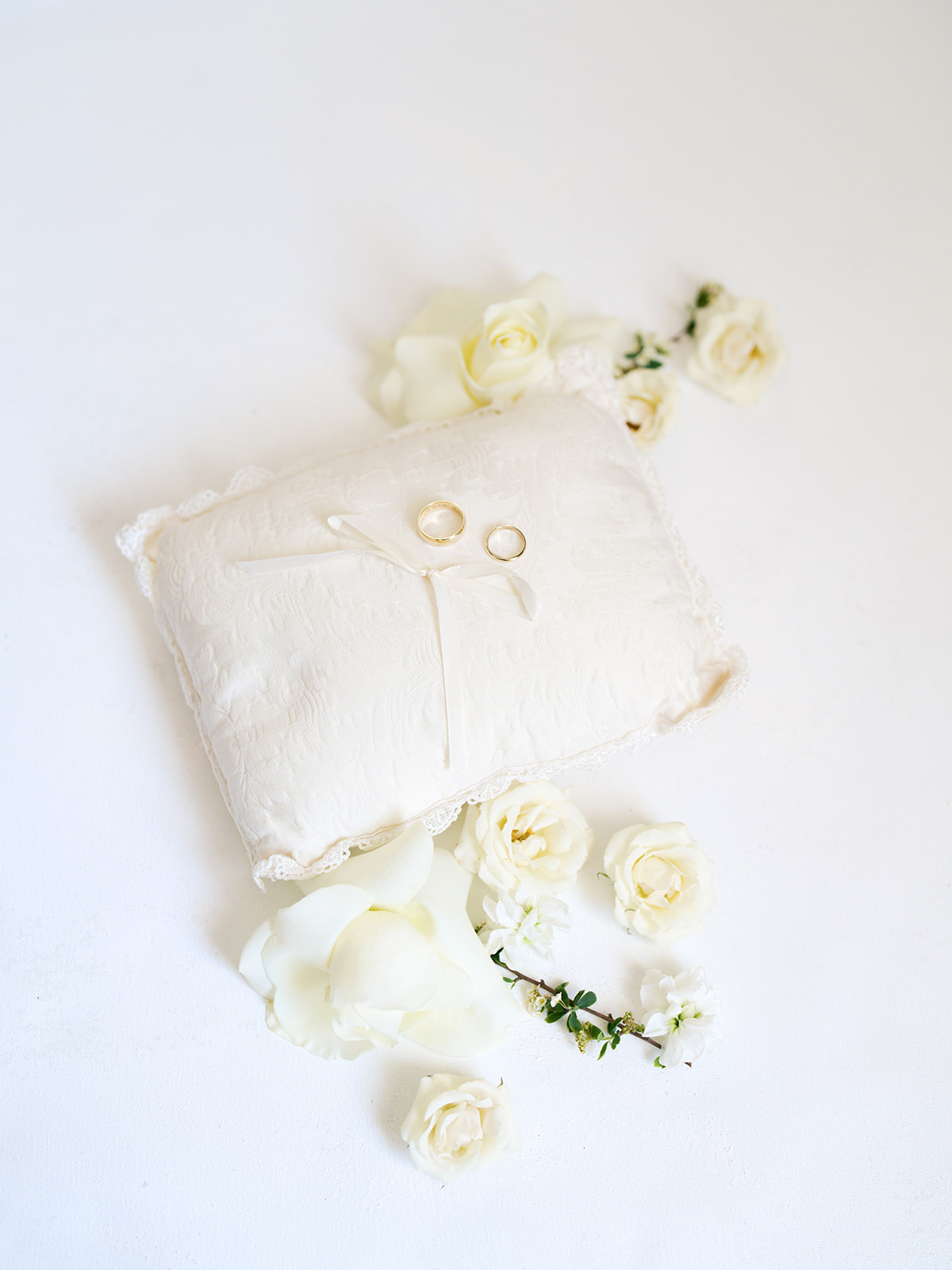 A white ring pillow with two wedding rings and ribbon, surrounded by white roses on a white background for a Houstonian Hotel Wedding