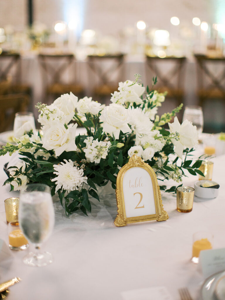 Elegant houston wedding decor with Long banquet table set with white tablecloths, plates of salad, wine glasses, and tall white candles in a bright, modern venue with large windows 
